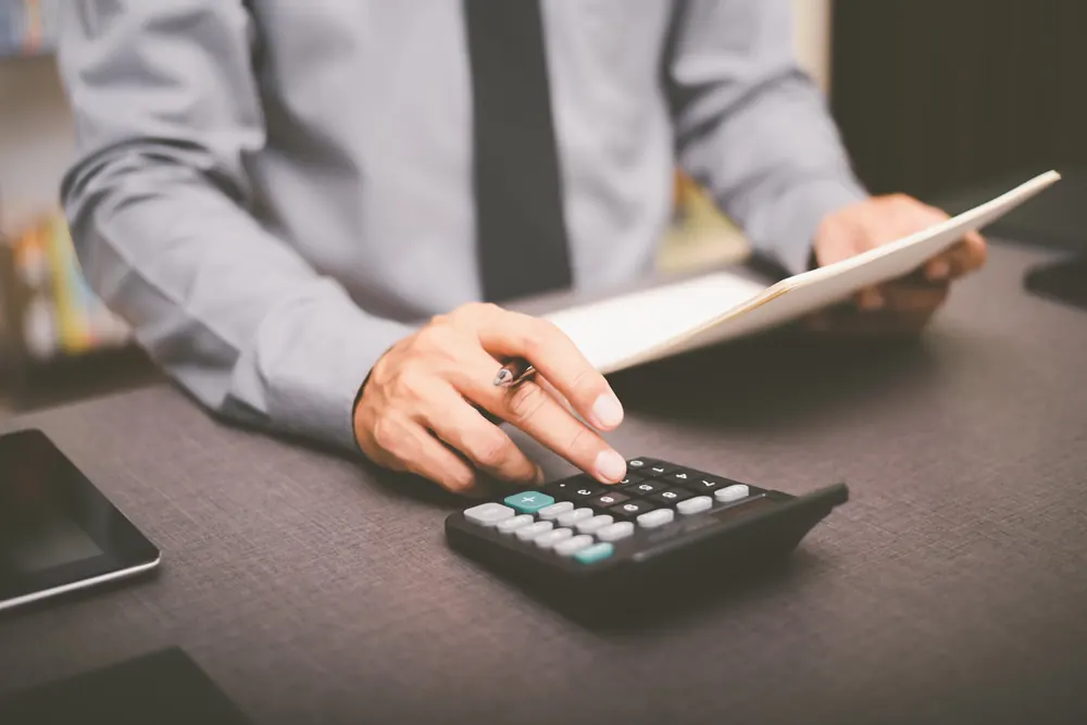 A hand using a calculator next to paperwork