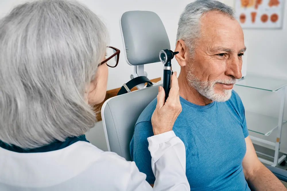 An audiologist checking an older man’s ear