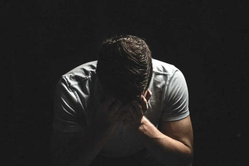 A man sitting in a dark room with his head in his hands