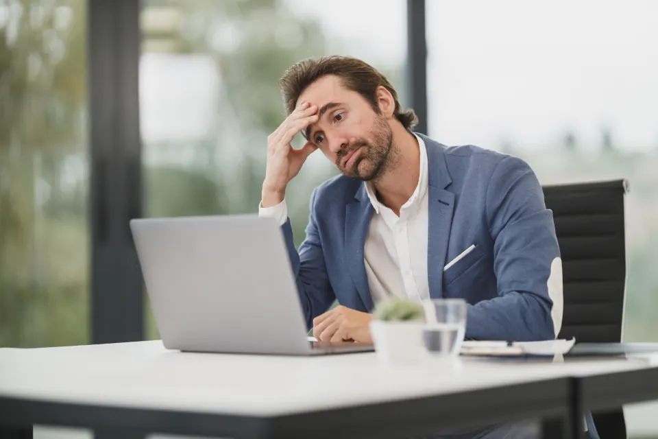 A man at a desk reading paperwork with his hand on his forehead