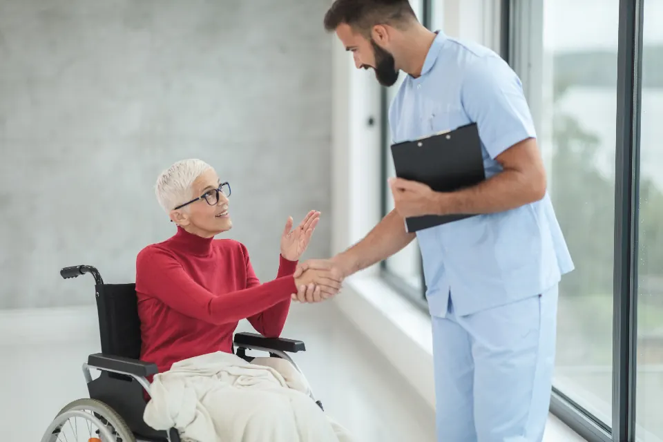A nurse shaking hands with an older woman in a wheelchair