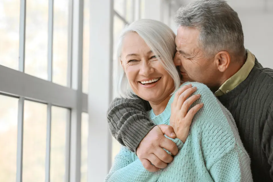 An older couple embracing by a window
