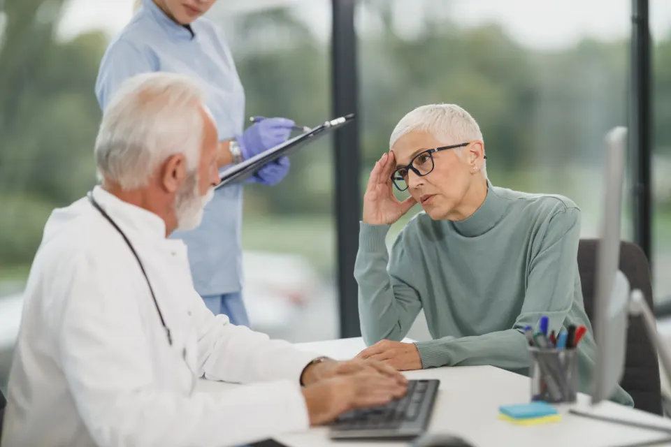 An older patient with a hand to her head talking with her doctor