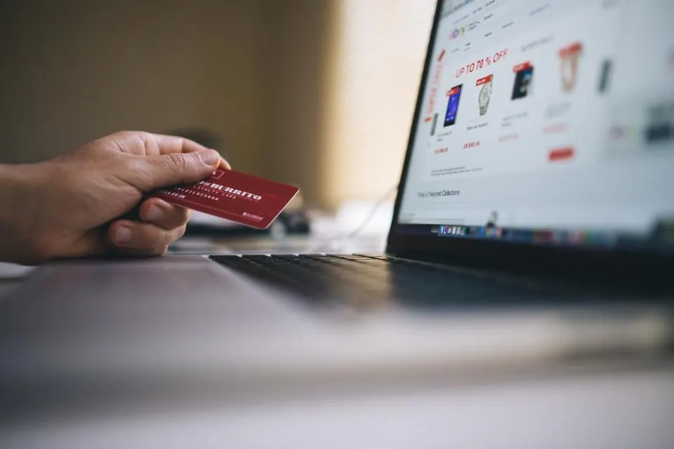 A hand holding a card next to a laptop