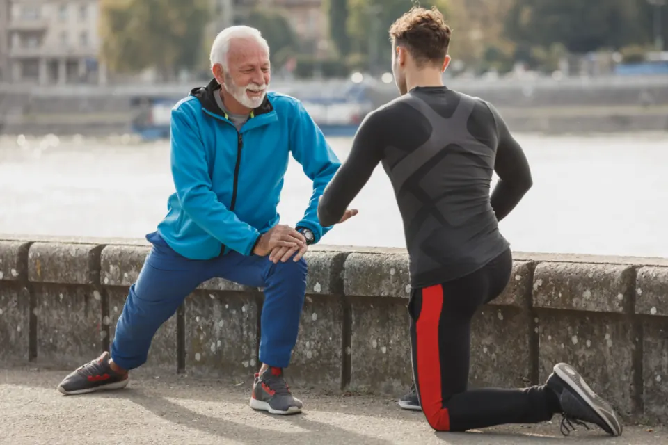 An older man doing a stretching exercise with a trainer