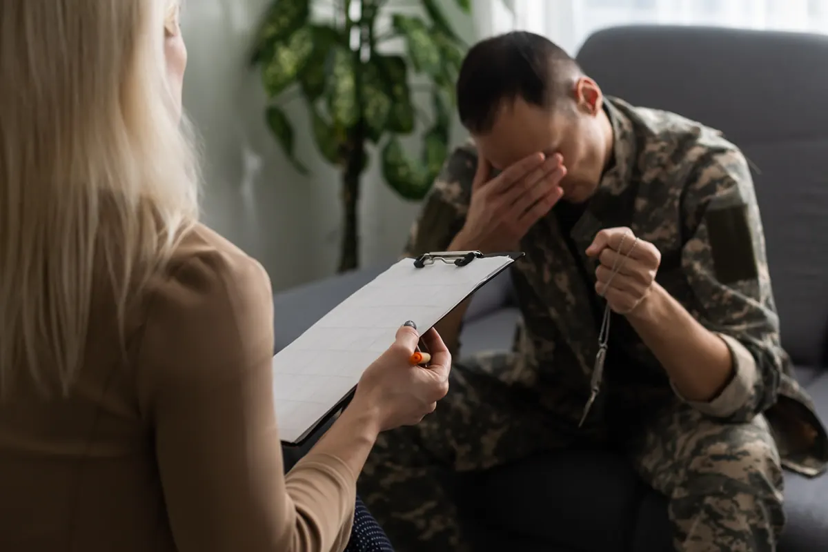A man in uniform with his hand over his face, talking with a counsellor