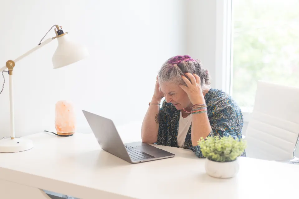 A woman at a laptop holding her head